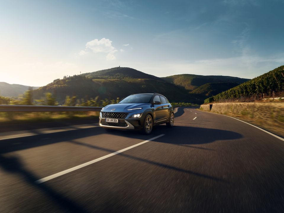 Vue avant du nouveau Hyundai KONA couleur Surfy Blue roulant sur une route de campagne.